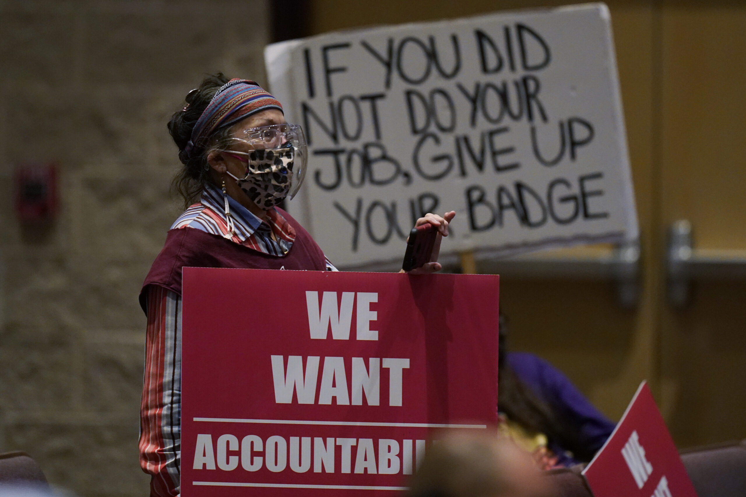 A protester holds a sign reading "If you did not do your job, give up your badge" at a meeting of the Board of Trustees of the Uvalde Consolidated Independent School District. A banner draped over the dais reads, "We want accountability."