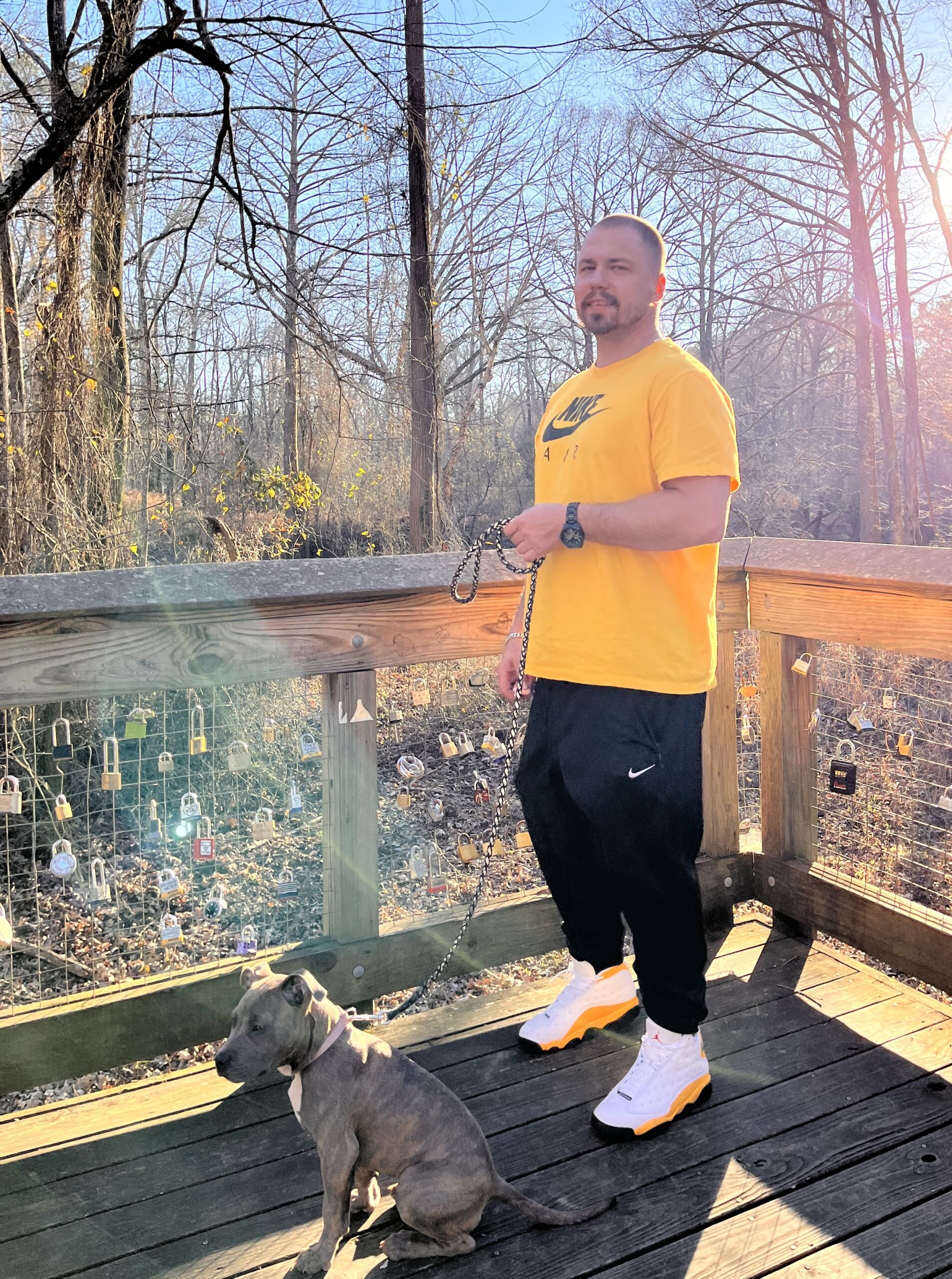 Clinton Young poses in a yellow Nike t-shirt and black Nike sweatpants, holding a small bulldog on a chain leash. He's outdoors on a porch in he fall.