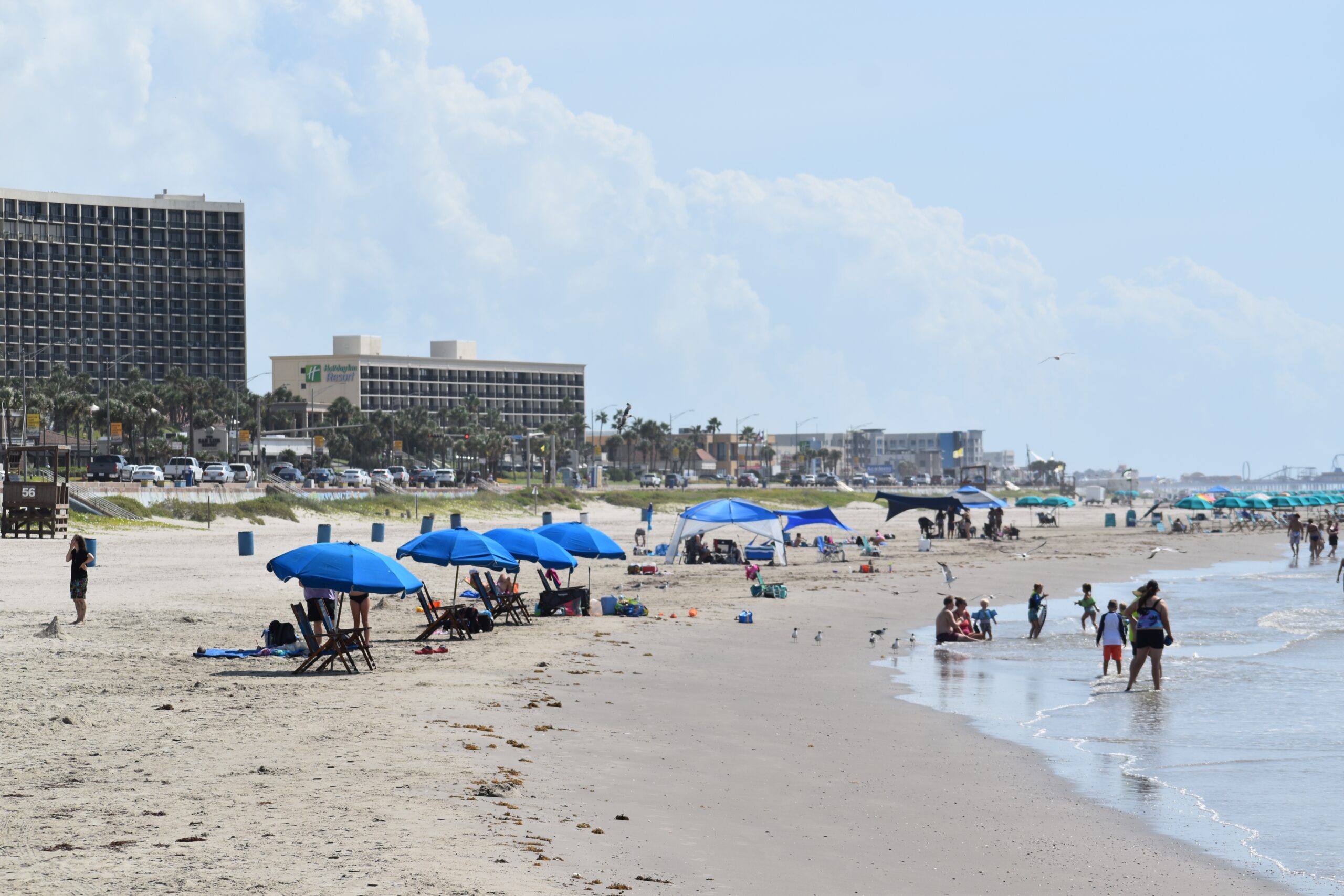 August summer in Galveston during a record-breaking heat wave. Beach goers cool off under rented umbrellas or in the ocean, with the beachfront hotels in the backdrop.