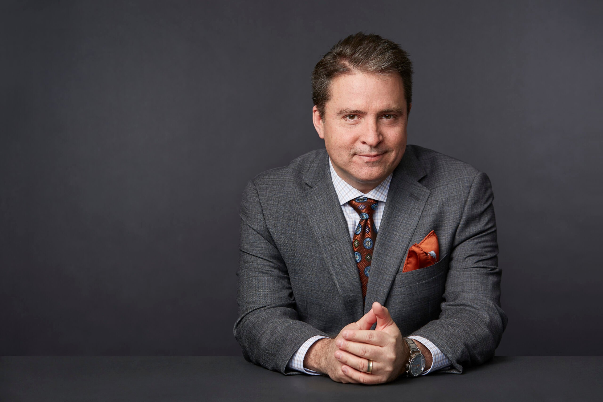 An image of author Robert P. Jones in a suit leaning on a desk with his hands clasped together