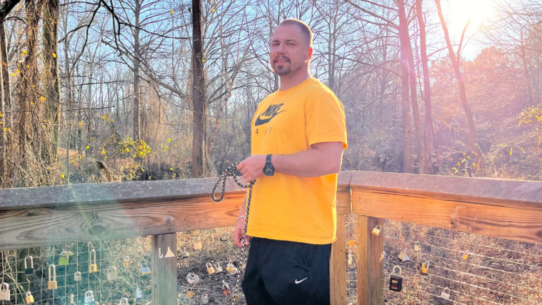 Clinton Young poses in a yellow Nike t-shirt and black Nike sweatpants. He's outdoors on a porch in he fall.