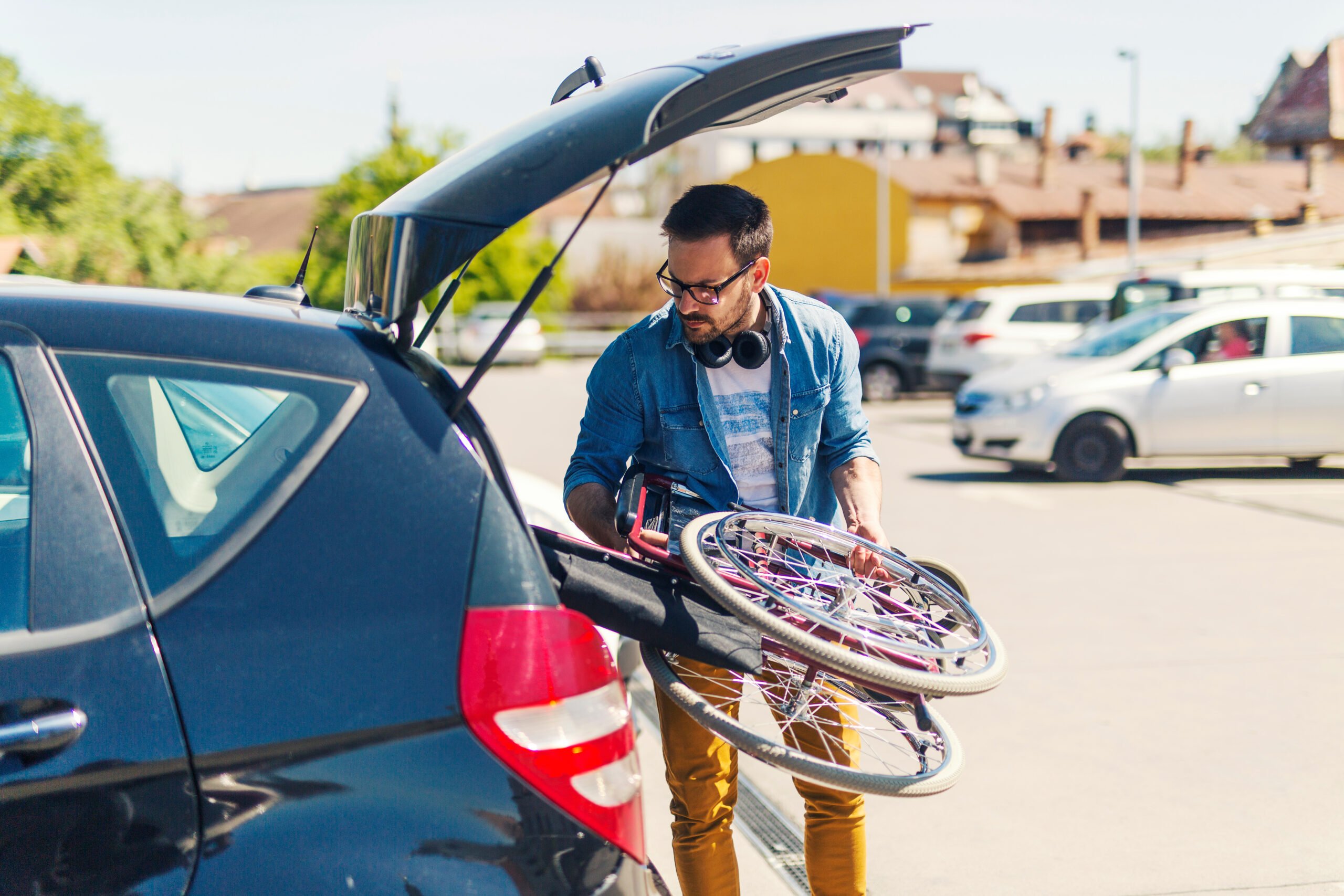 A young adult loads a foldable wheelchair into the back of a sedan type car. Personal community-based attendants wages are pegged at a shockingly low $10.60/hour.