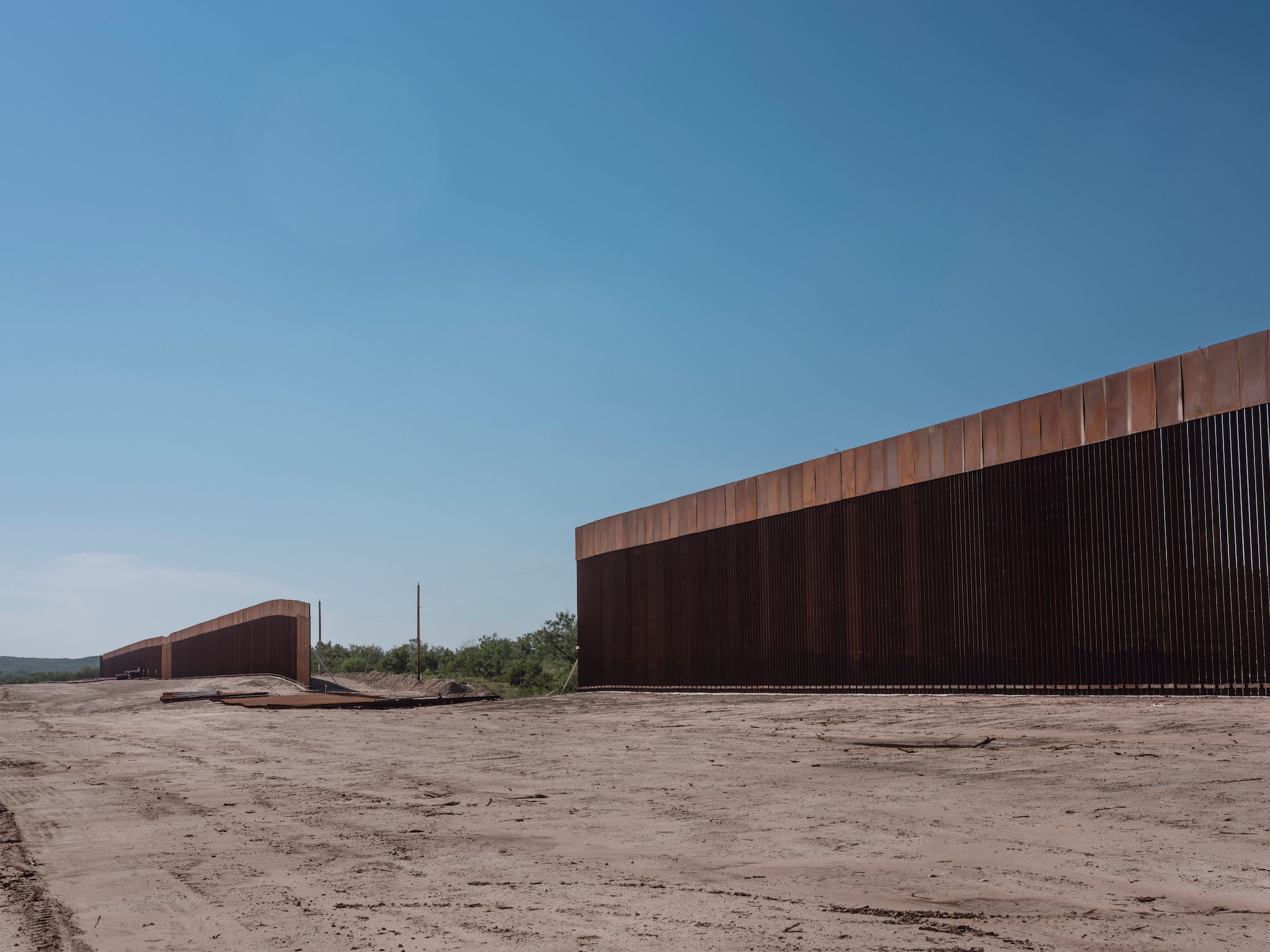 A section of the border wall in Del Rio, Texas. There is a large gap where the wall is unfinished. It is surrounded by dusty desert and low plants.