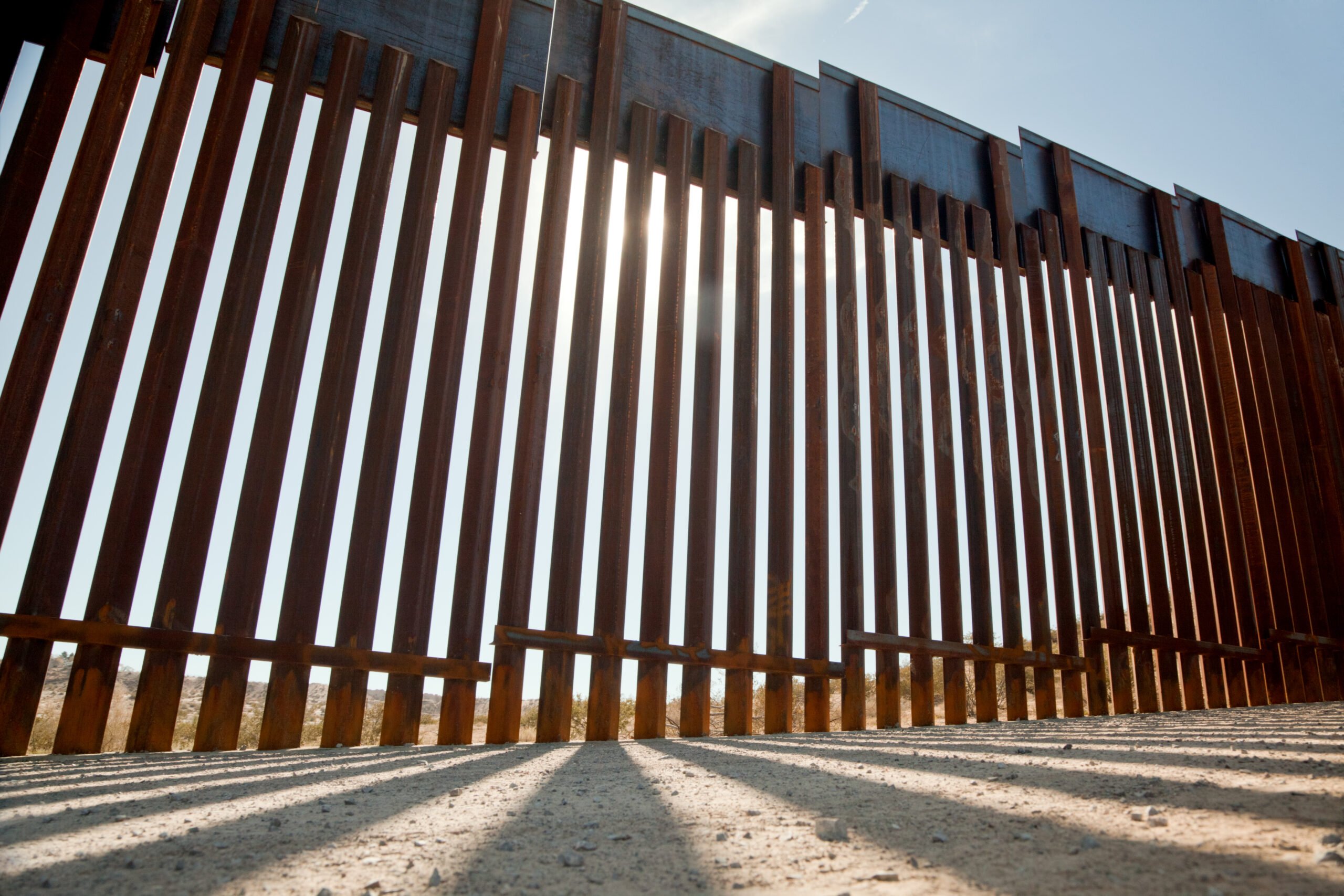 A ground level view of the wall at the U.S / Mexico border, standing under the sun in the desert.