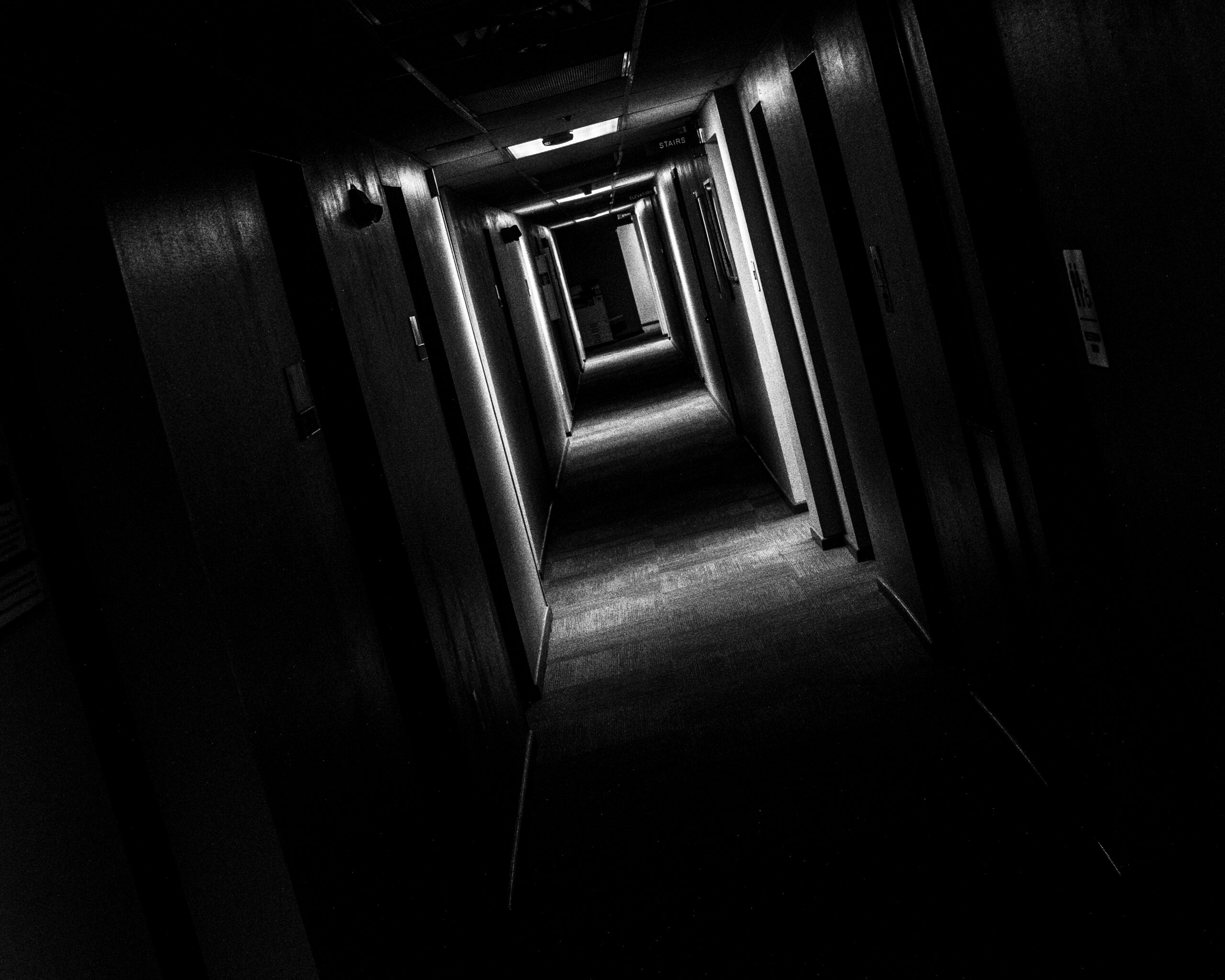 A diagonally angled shot of a long hallway, alternately seen in light and shadow in rough rectangular patches heading away from the viewer. At the former Confederate Women's Home