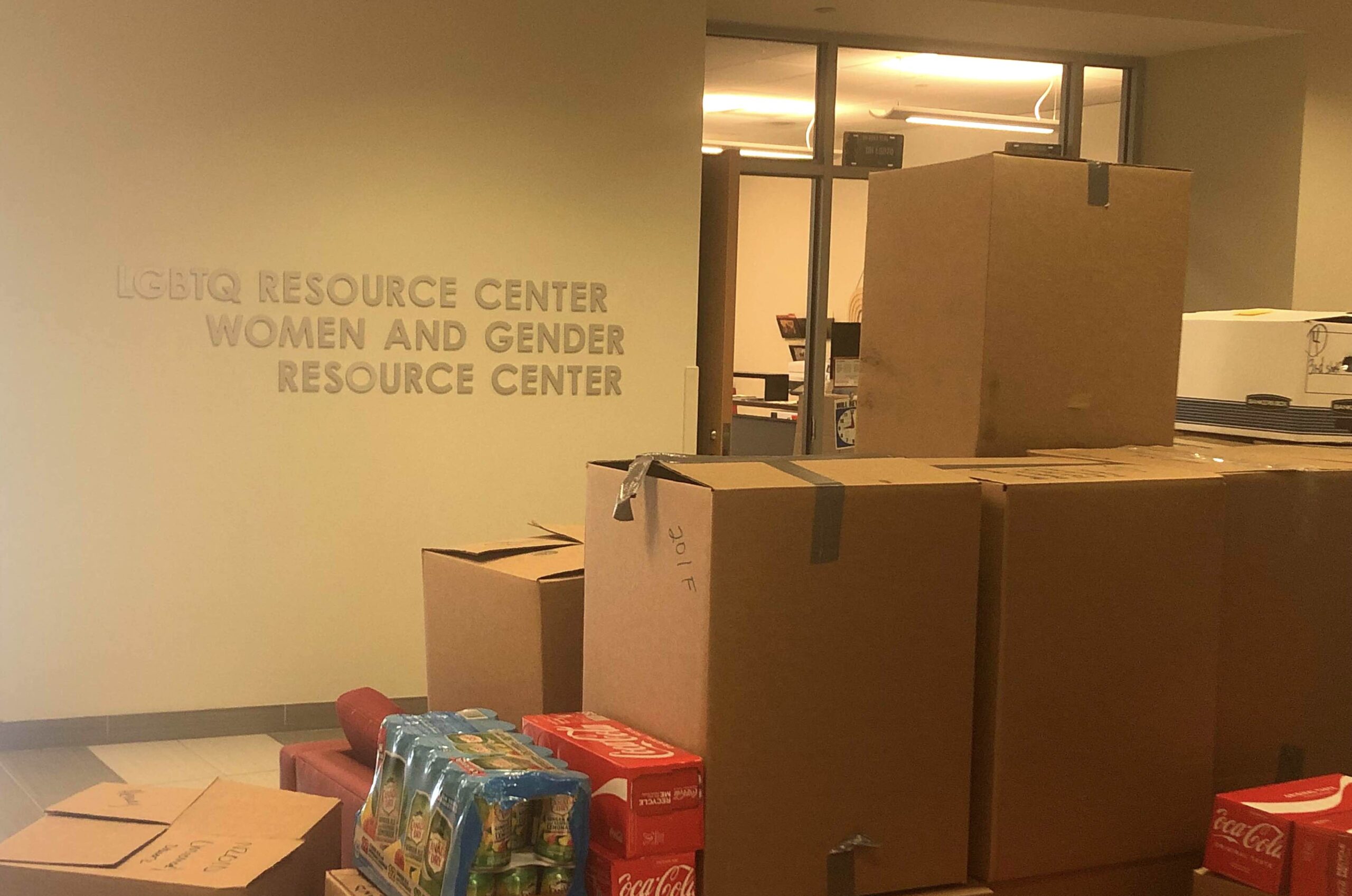 Stacks of cardboard boxes contain the contents of the LGBTQ+ and Women and Gender Resource Center. Letters on the wall describe what the space once was.
