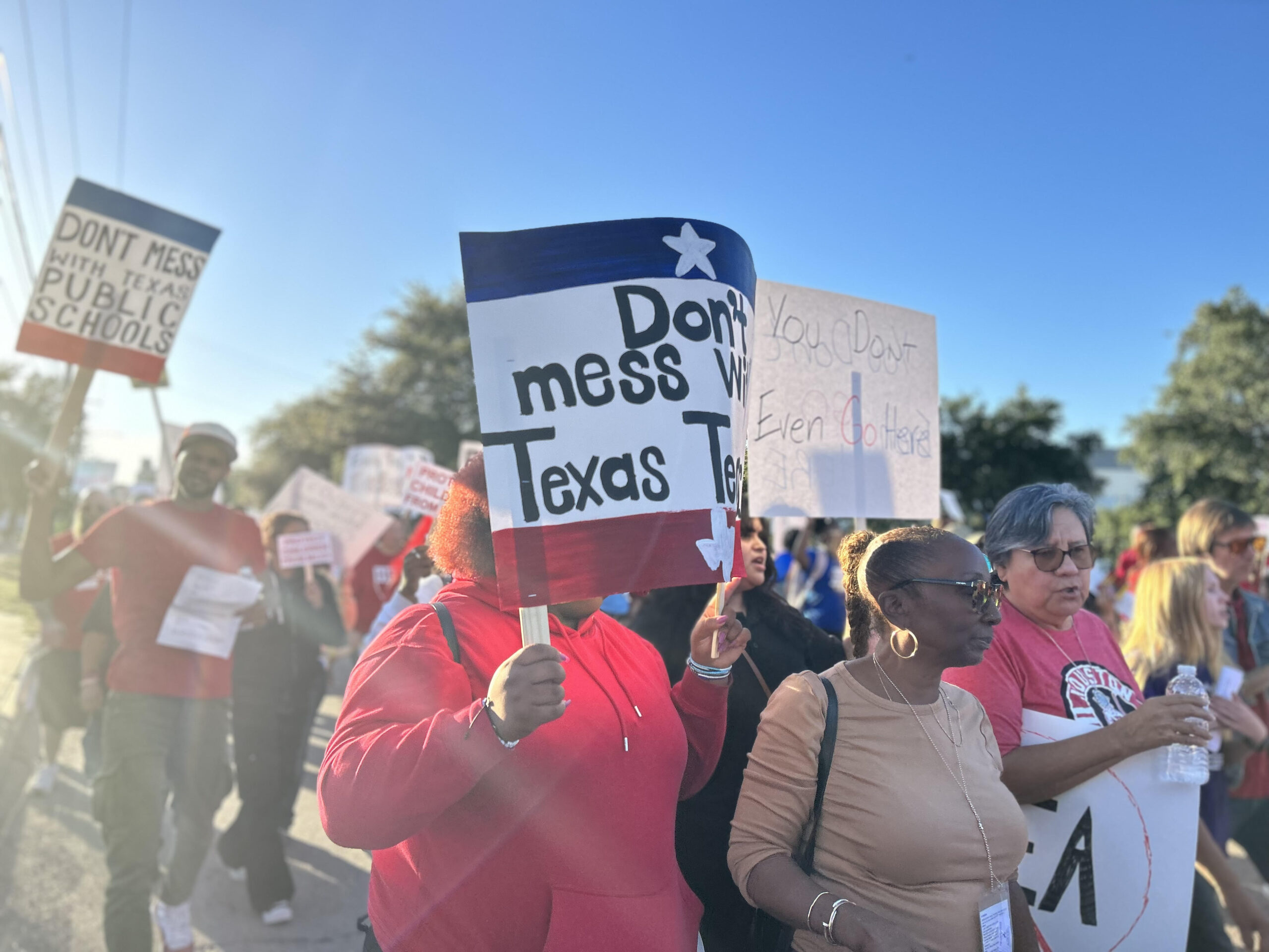 A diverse crowd marches against the takeover of Houston ISD. In front are two Black women, one holding a Don't Mess With Texas Teachers sign.