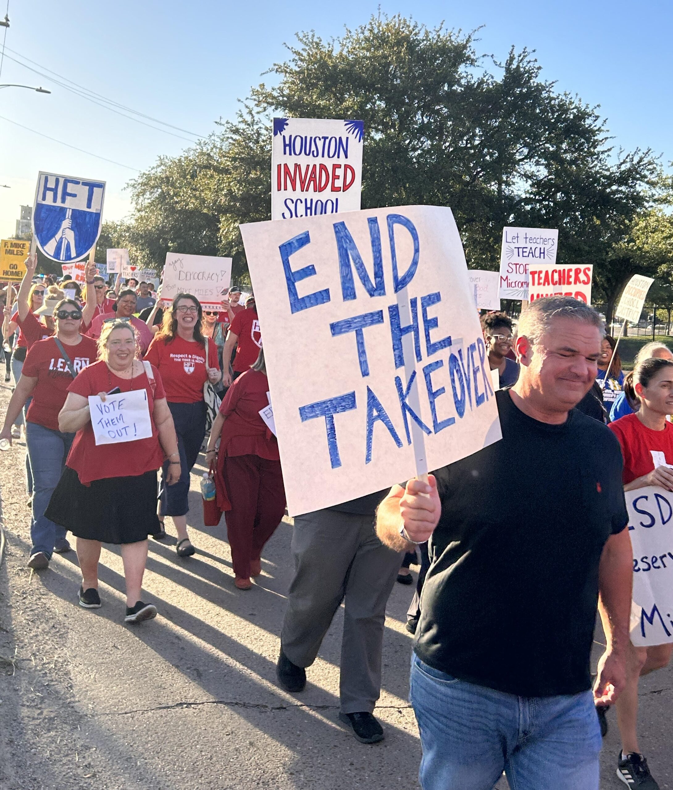 A dense crowd, most wearing red t-shirts, march with signs protesting the state take over of Houston ISD.
