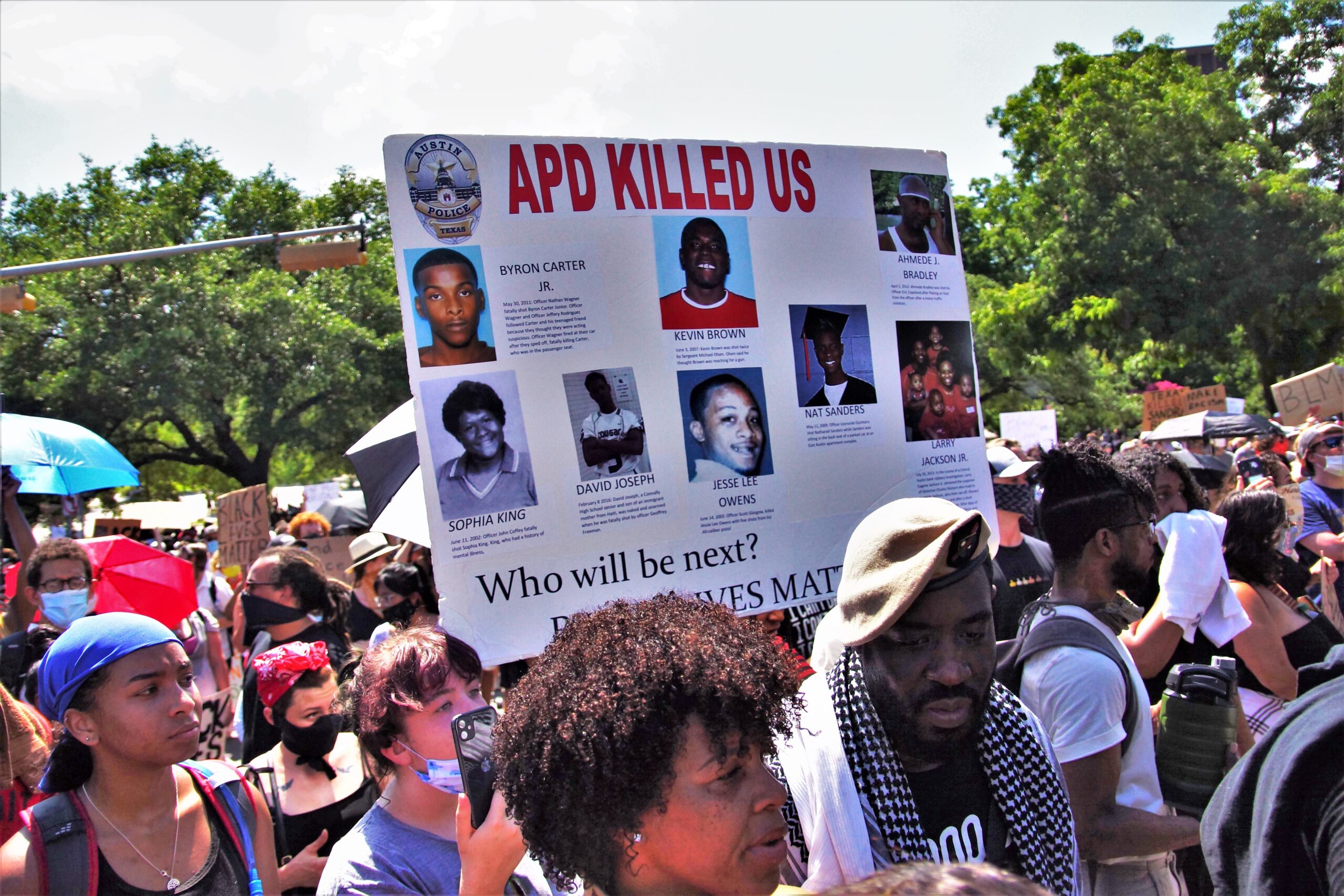 Scene of a protest focused on a sign that reads "APD Killed Us" along with images of victims of police violence