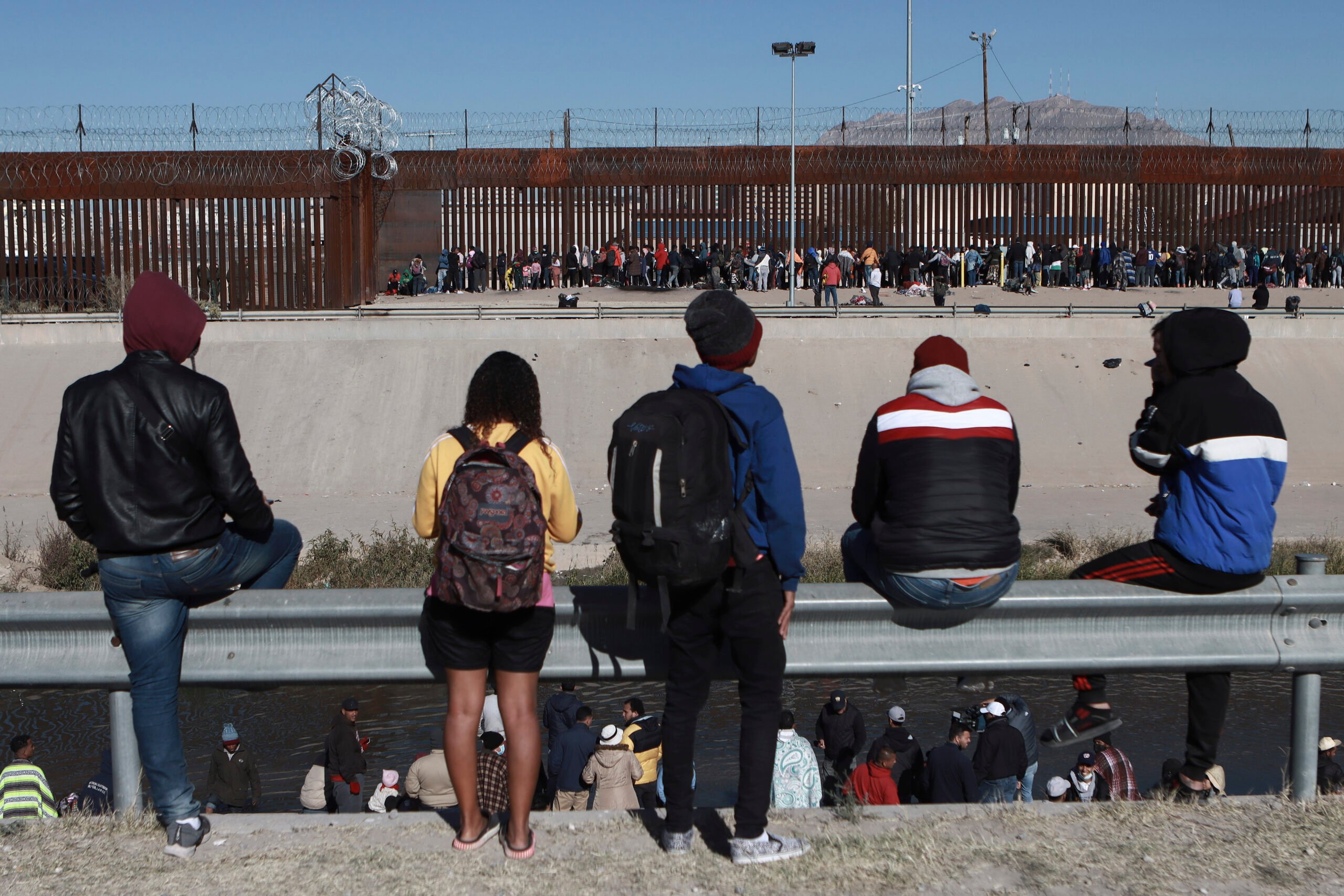 Migrants watch others stand next to the border wall in Ciudad Juarez, Mexico.