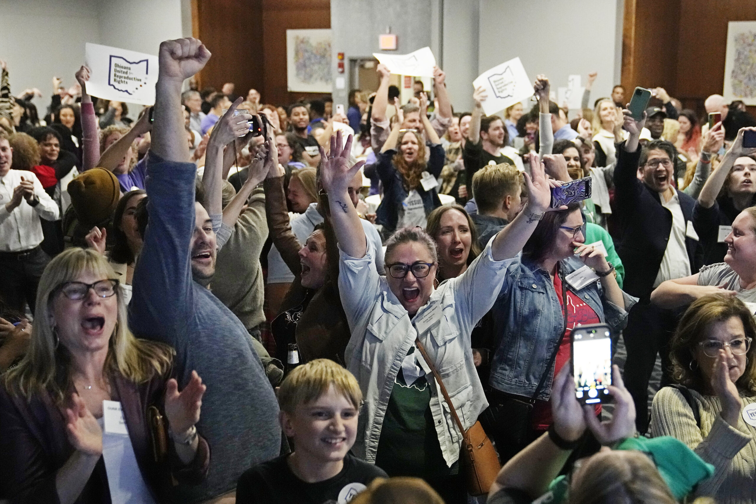 A room full of Ohioans with their arms raised in celebration