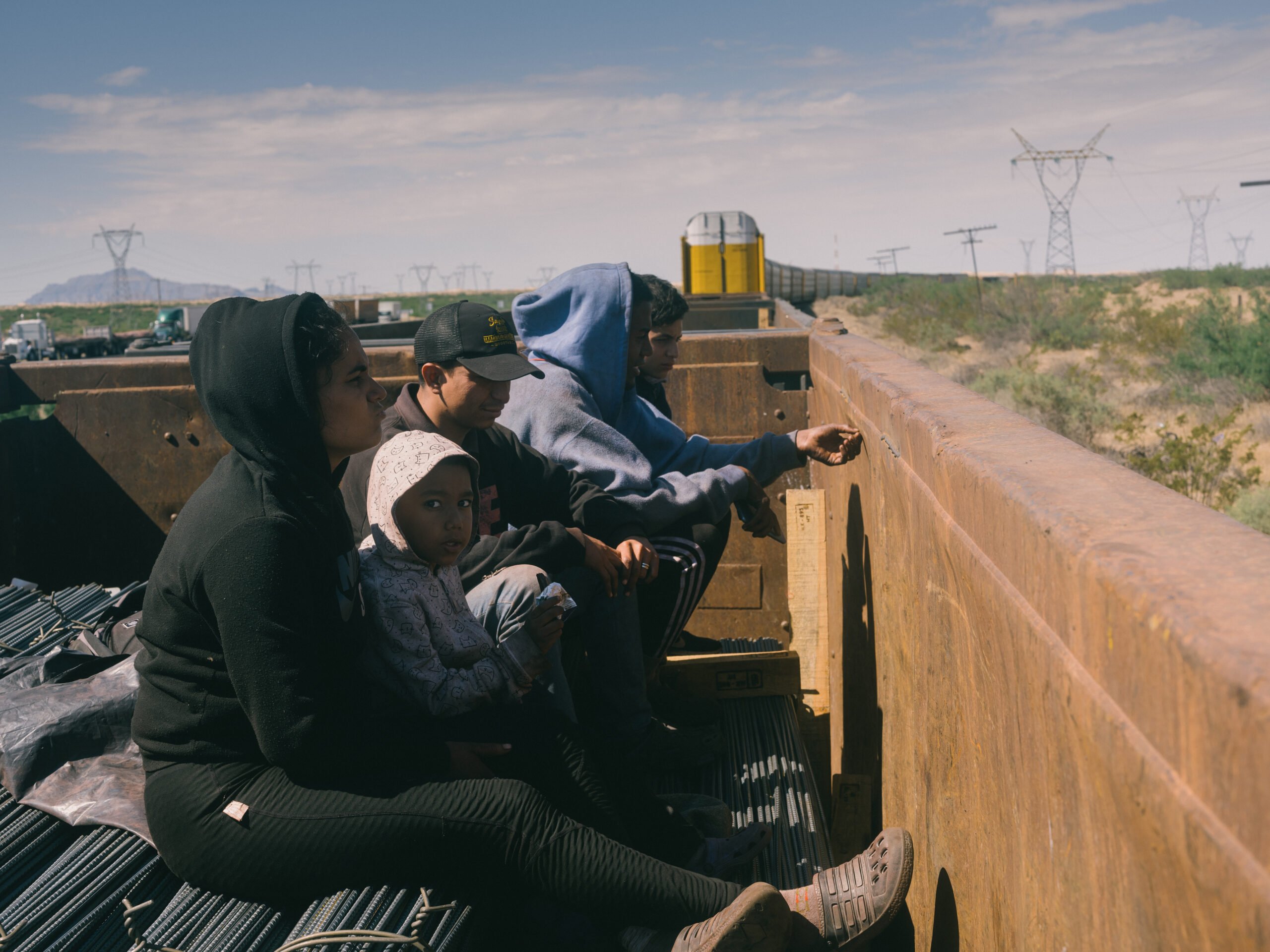 The four member family uncomfortably half sits, half squats atop the rebar bundles, one bracing himself against the wall of the train car. The spiky metal twist ties surround them as the train moves rapidly through the scrub-filled desert.