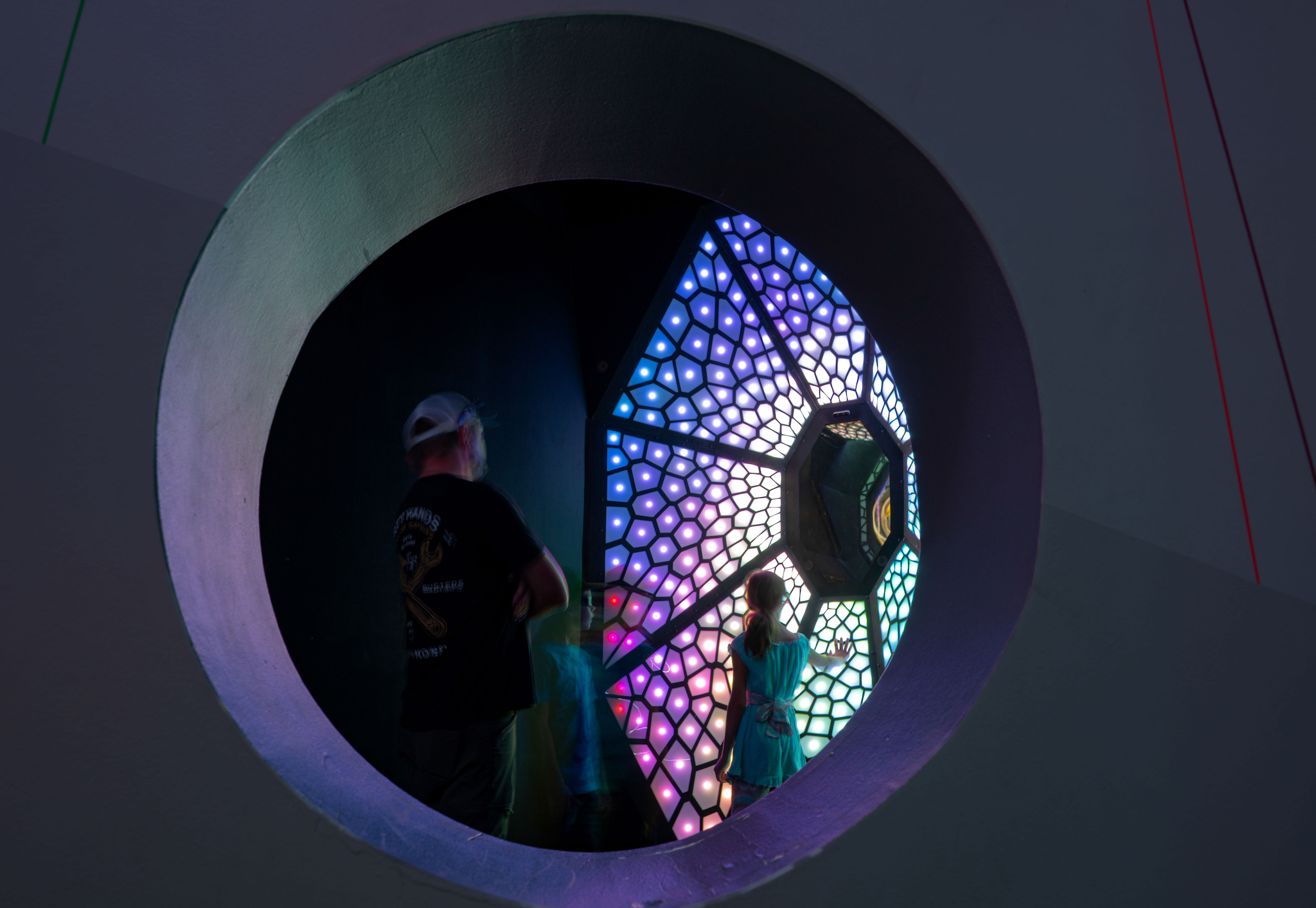 A large round opening in a wall at Meow Wolf Grapevine opens onto another artwork, an immense circular stained glass piece looking a bit like an eye or a flower.