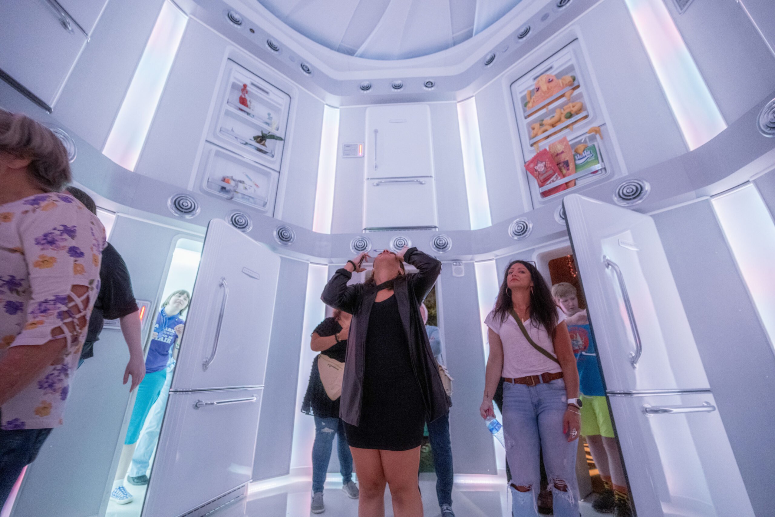 A trippy hexagonal room inside Meow Wolf Grapevine, made of two stories worth of refrigerator doors. Visitors explore the doorways, some wearing light refracting glasses.