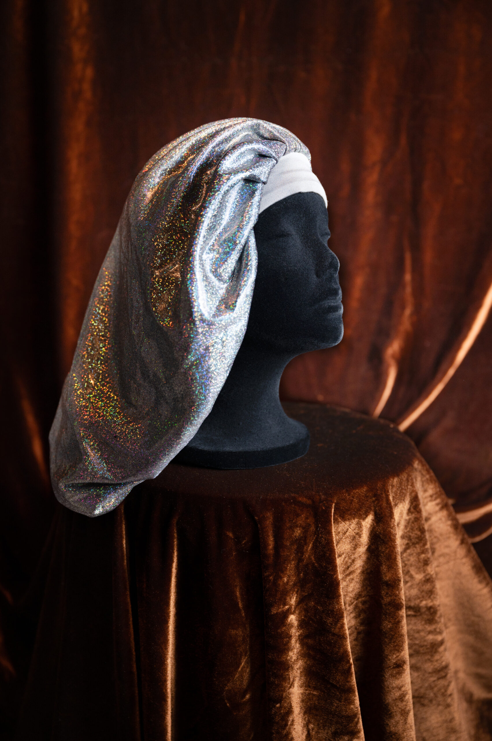 A mannequin head wearing a bonnet made from shimmery silver blue fabric.