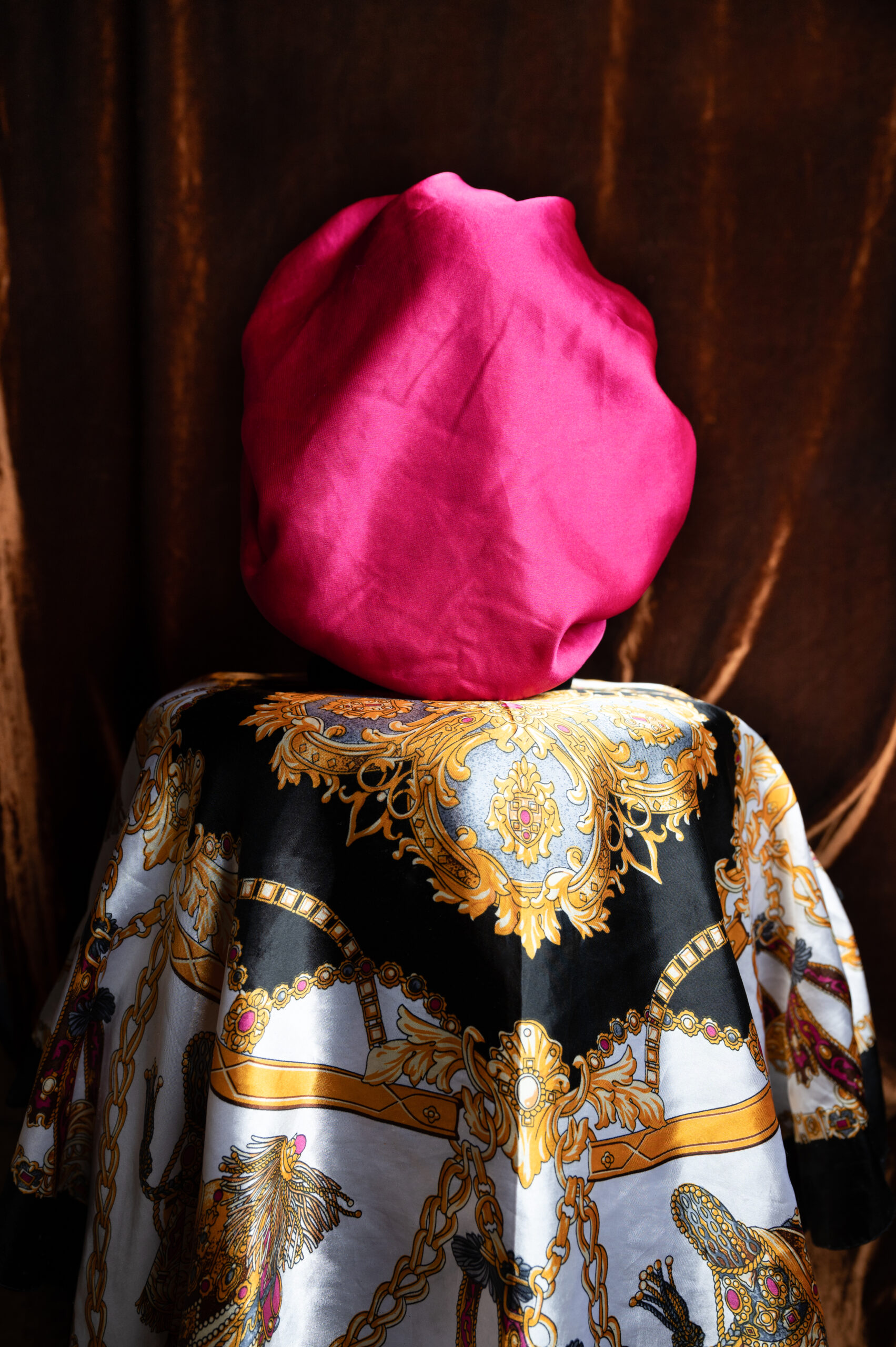A bright pink bonnet resting atop a table covered in an elegant patterned scarf.