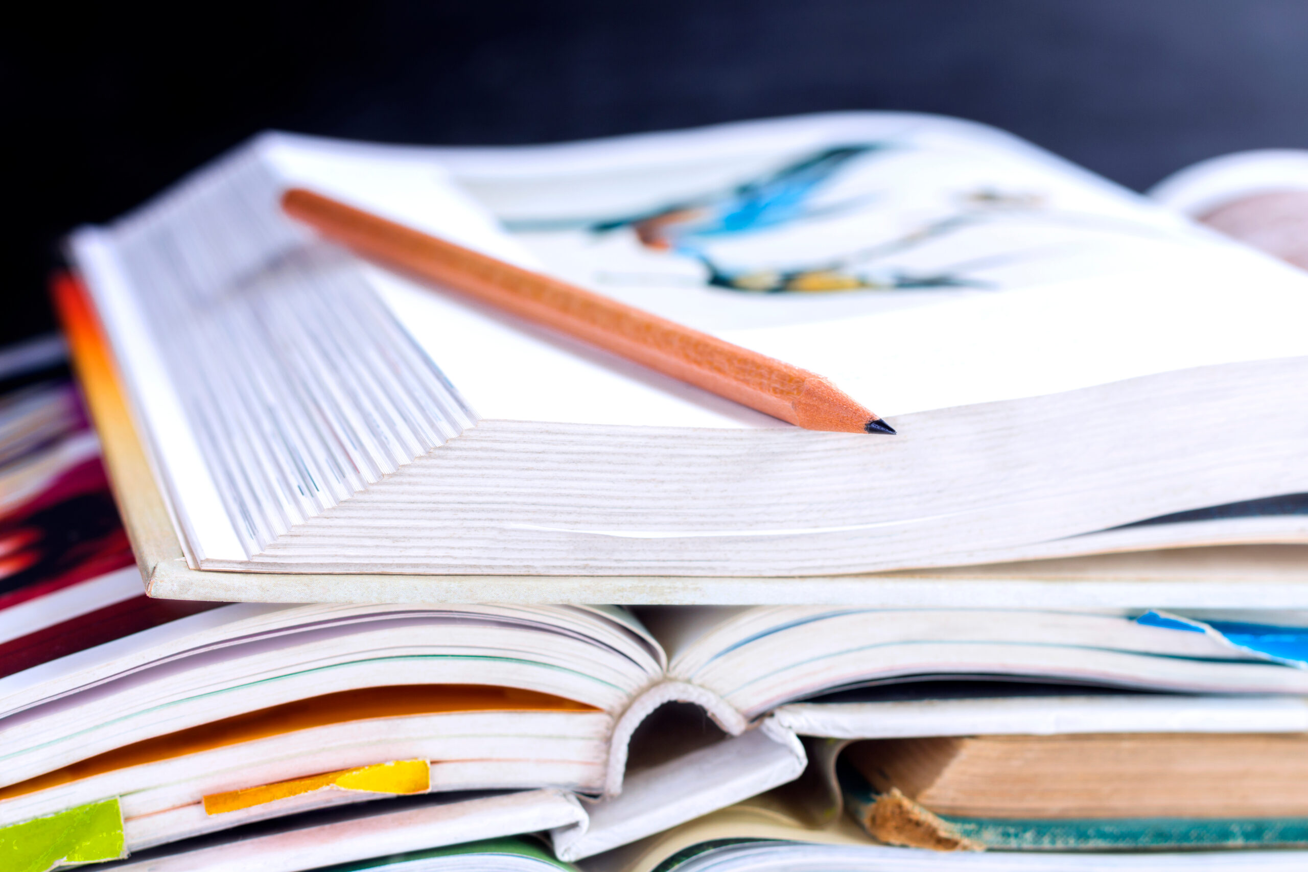 A haphazard pile of open, used textbooks, seen from the top edge of the books, with a pencil across the open page of the top textbook.