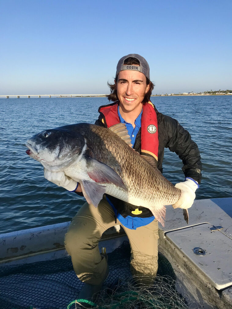 Philip Souza holds a massive silvery gray fish. He's wearing a backwards ball cap and a red vest.