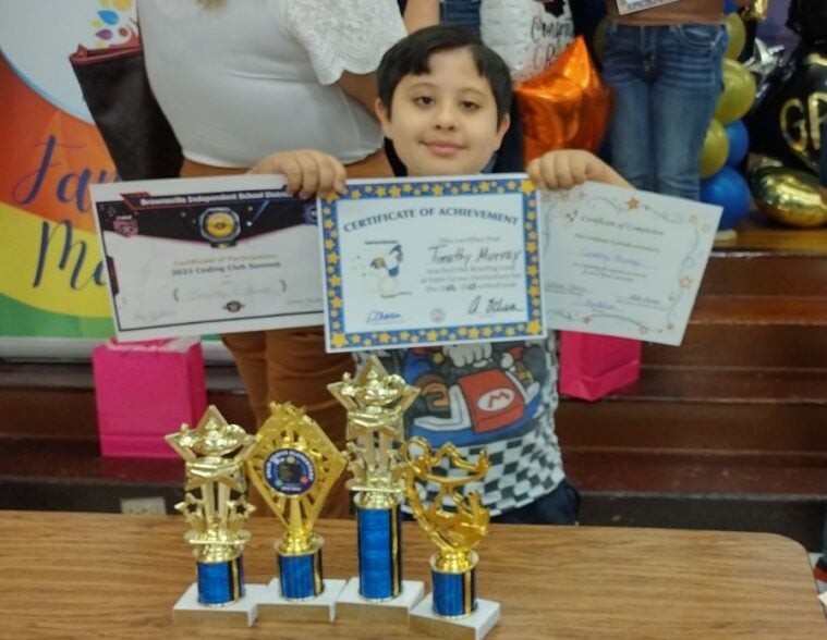 Timothy holds up three certificates and four trophies