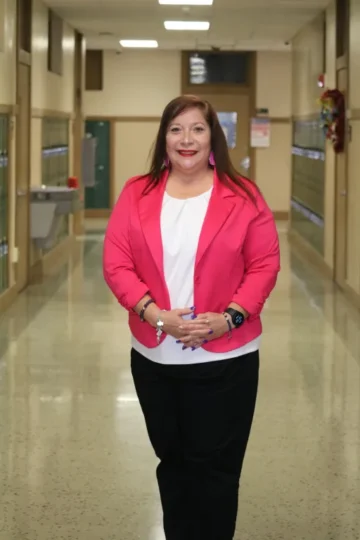 Palm Grove Elementary School Principal Myrta Garza stands in a school hallway with a pink blazer and black pants. 
