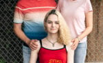 Trans youth with the arms of parents around her