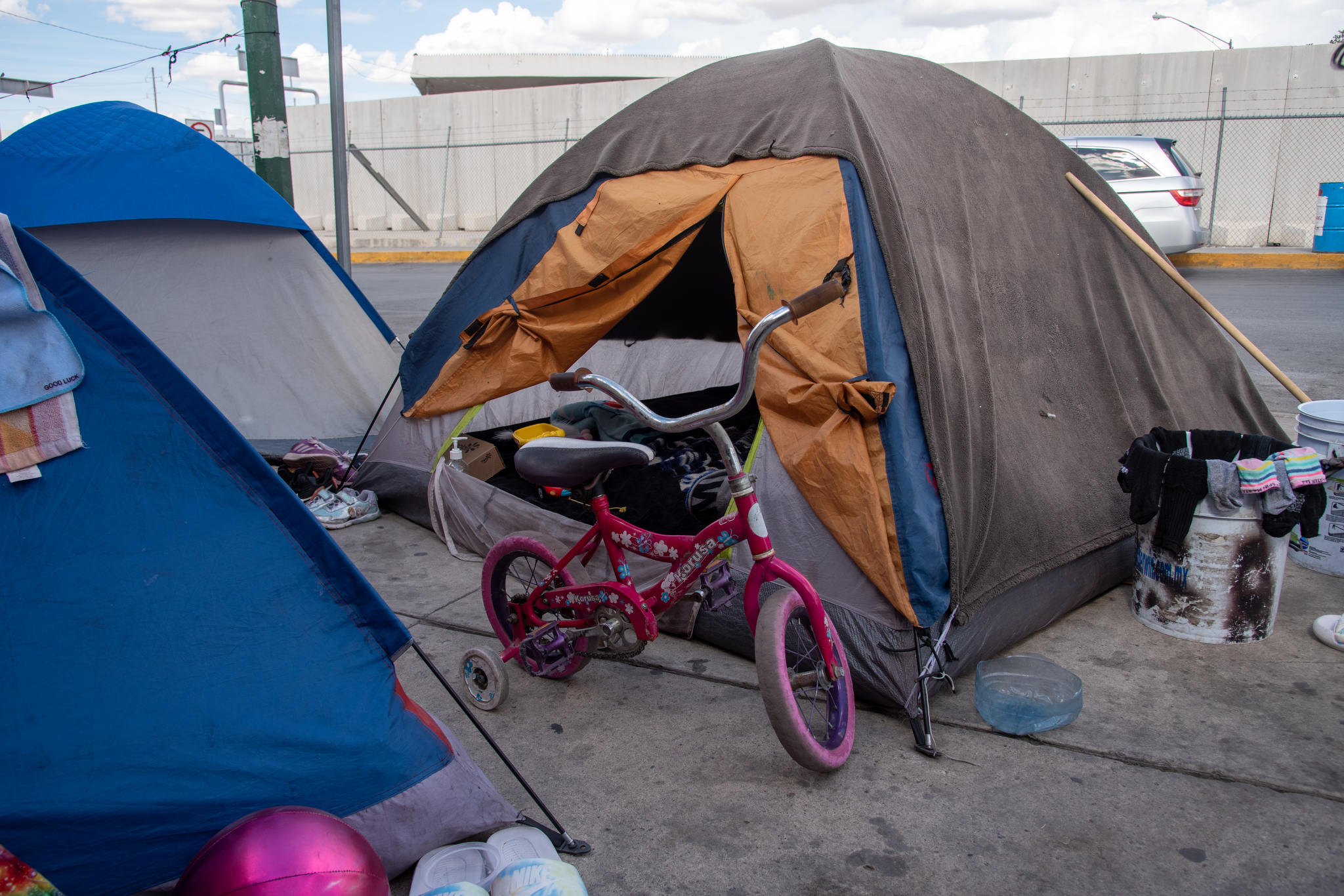 A girl's pink cruiser bike sits among tents on a sidewalk, overflowing with personal possessions. 