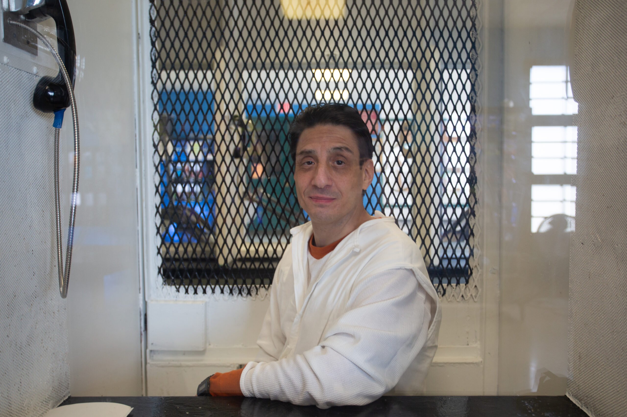 Ivan Cantu in a white jumpsuit in front of a metal screen