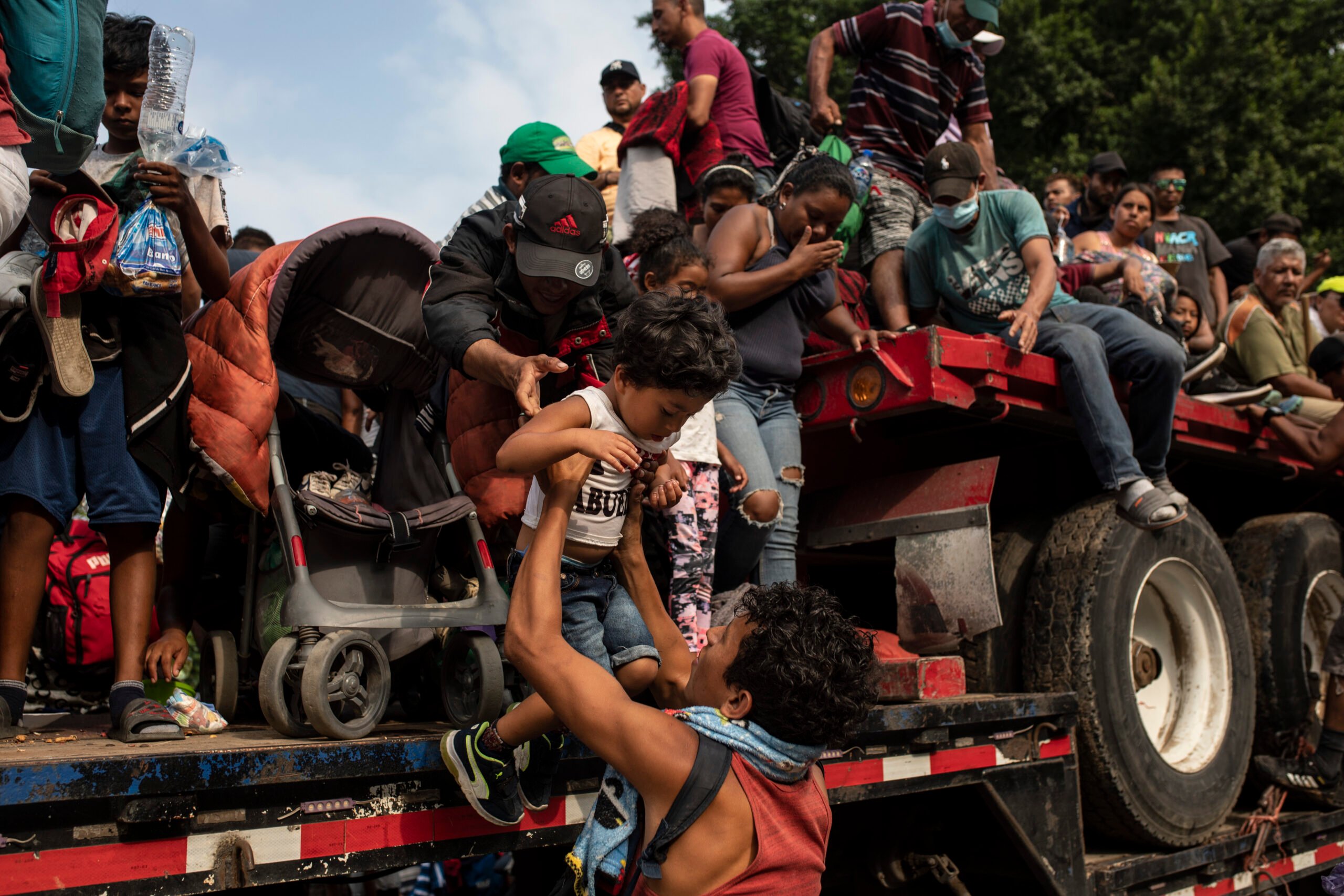 A child is being picked up off a crowded trailer covered with migrants
