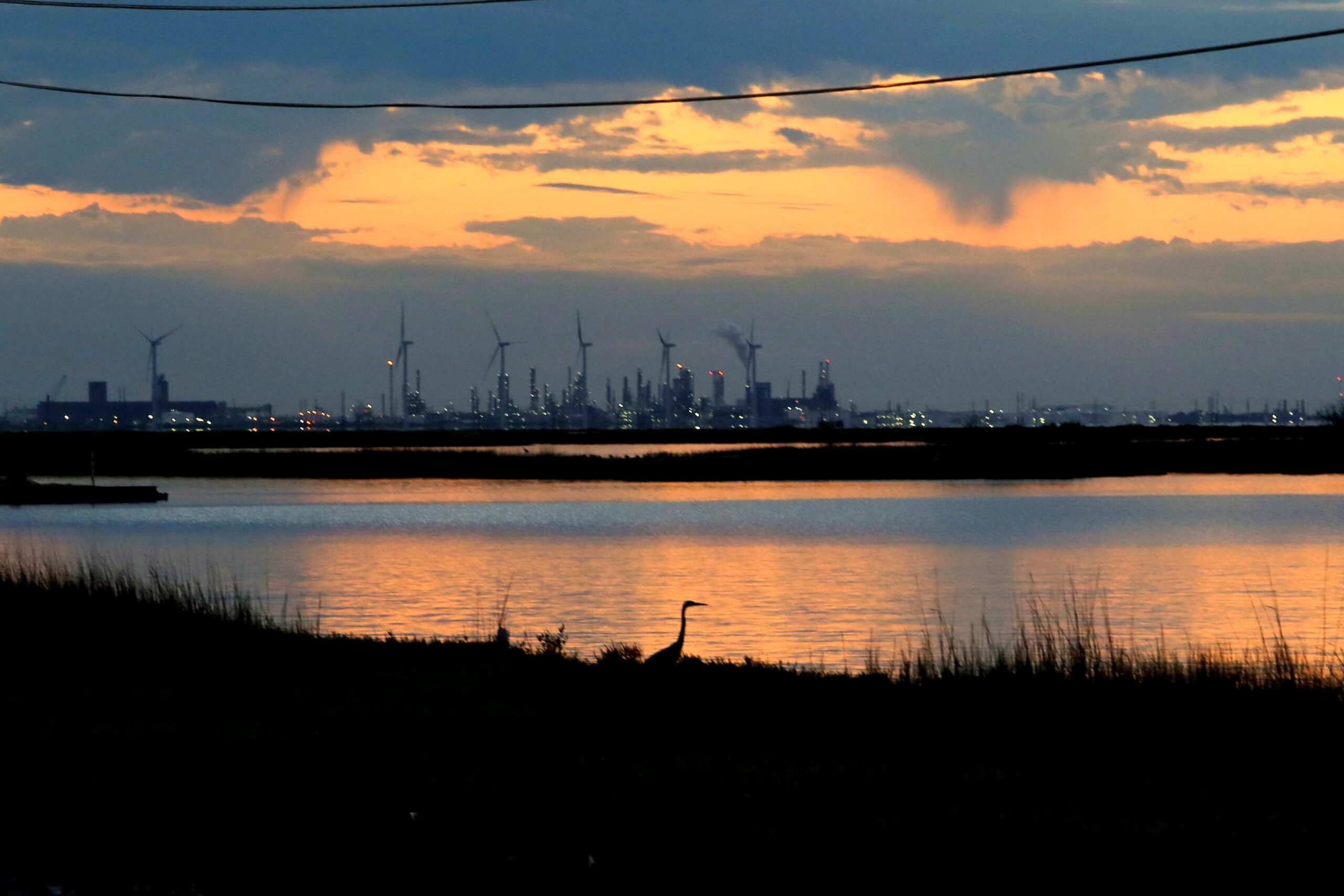 The sun is setting over the refineries and windmills along Nueces Bay