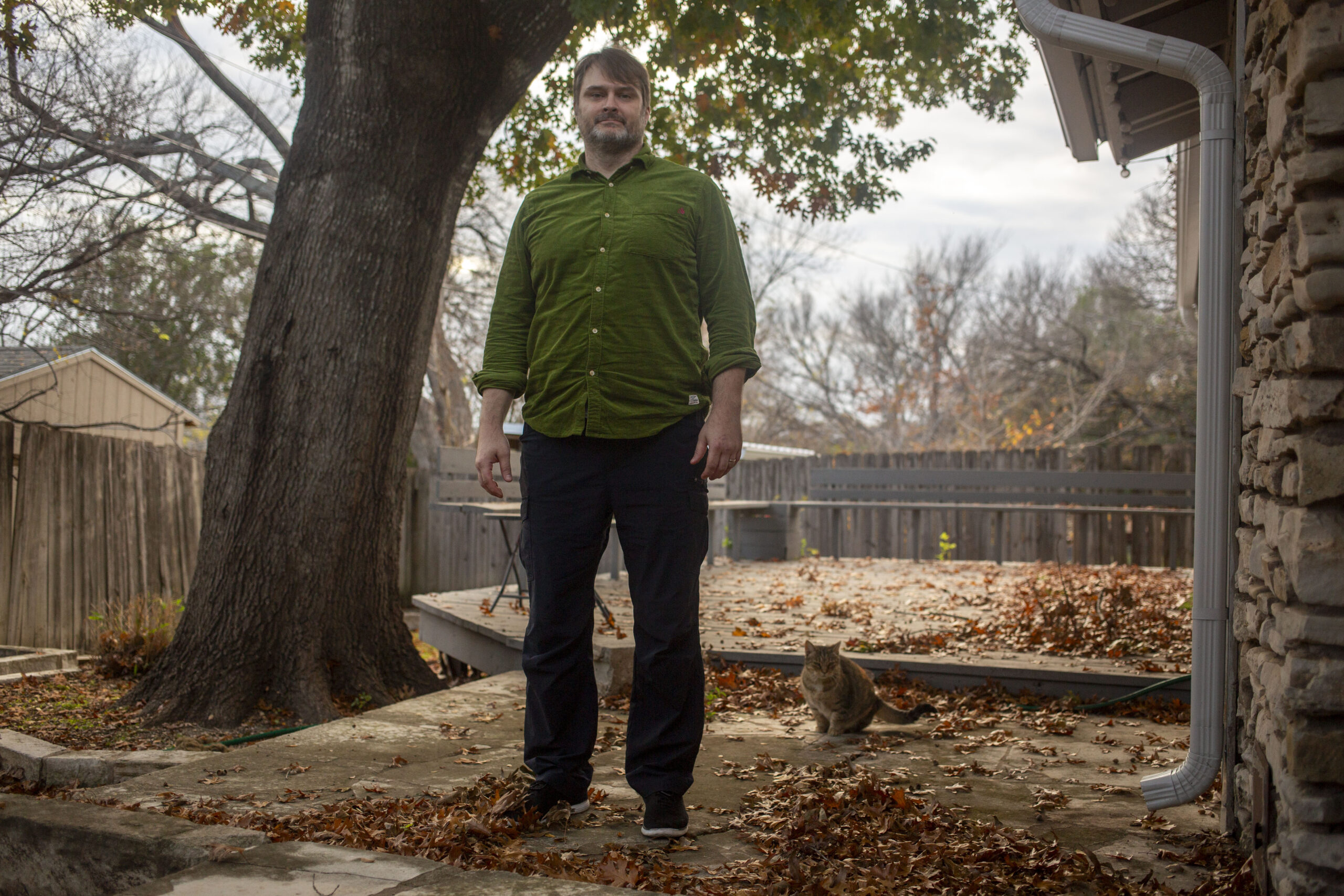 Gabriel Clark-Leach is a white man with short brown hair in a green button-down, standing in a back yard.