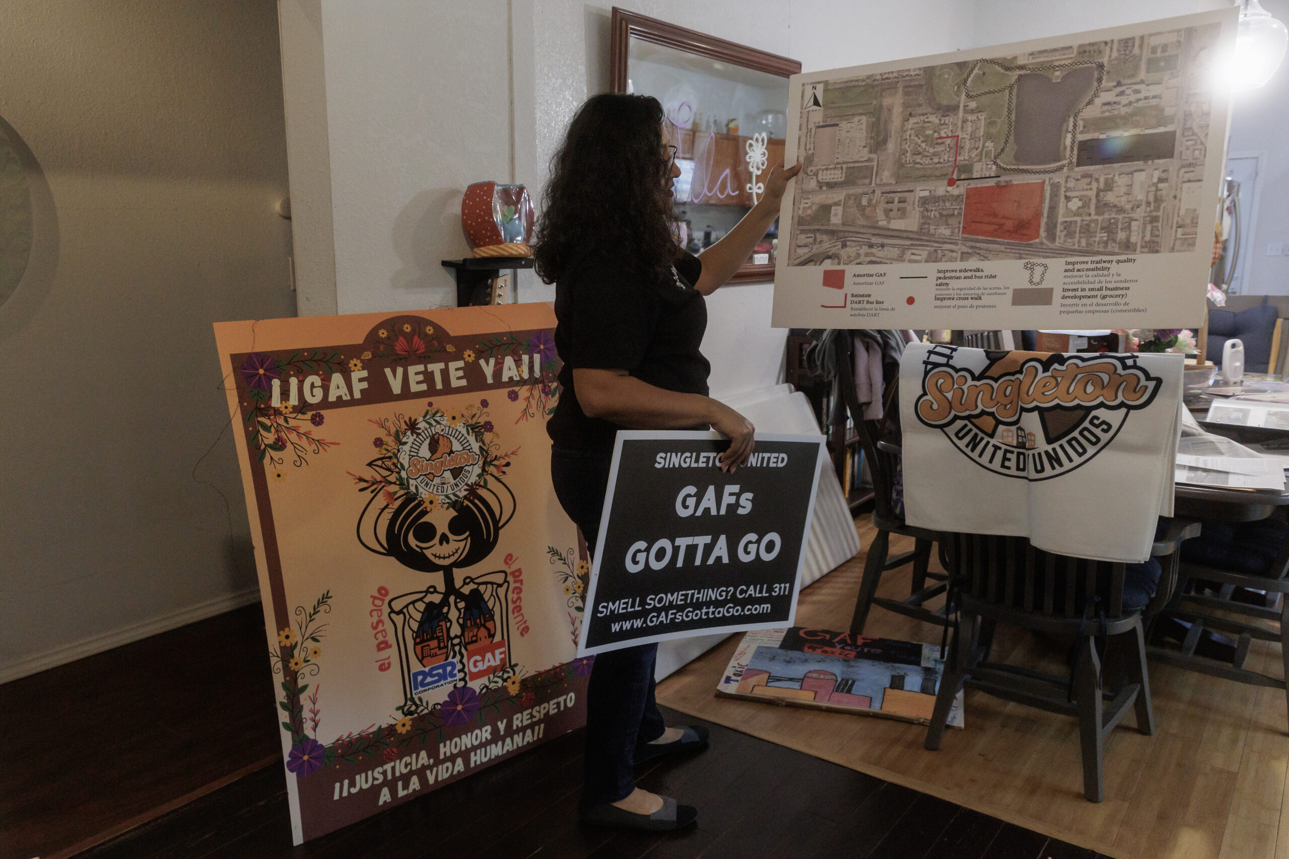 A Latinx woman displays various signs and printed infographics, on stands inside of her living room.