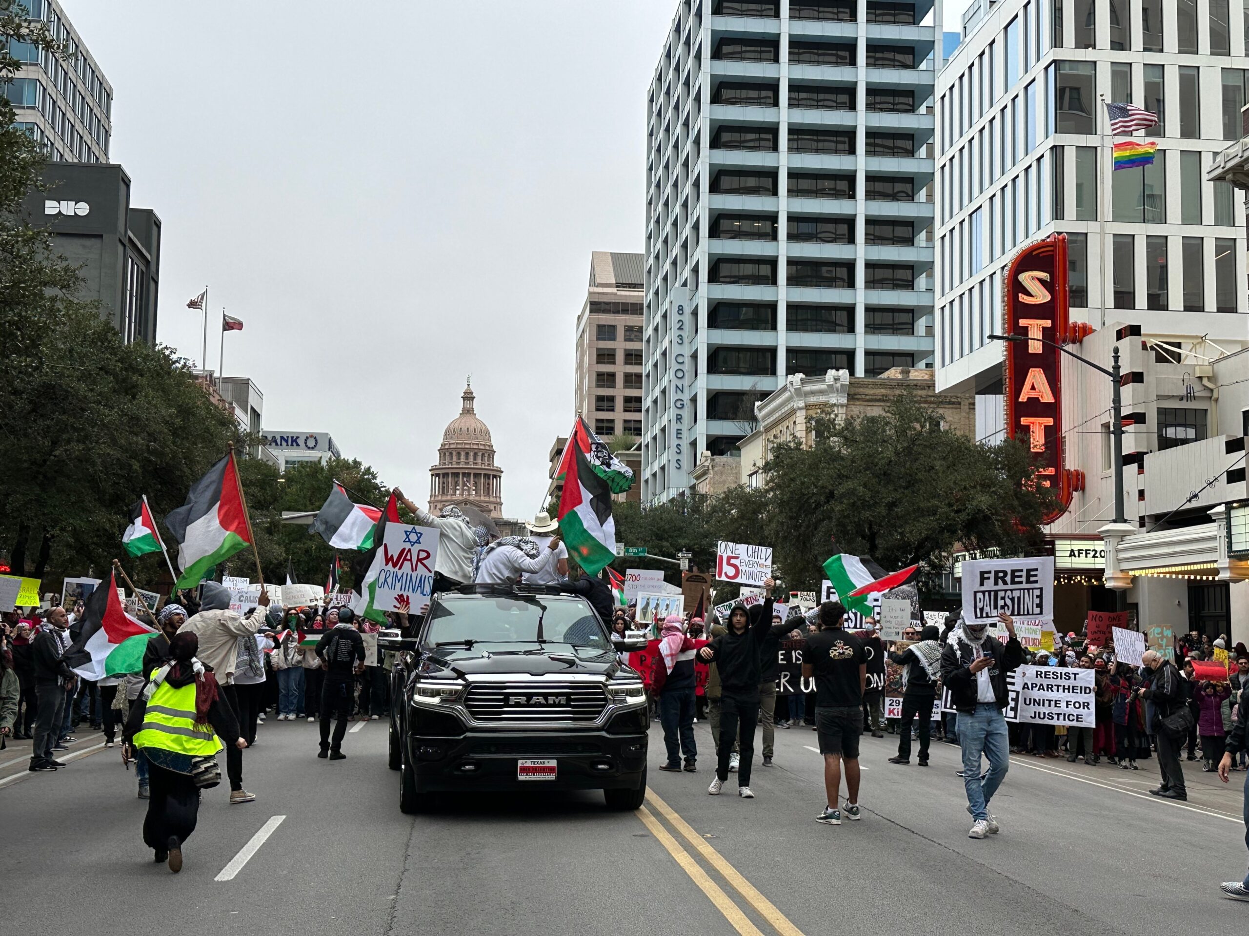 Thousands march with Pro-Palestine signs and Palestinian flags in a protest demanding a ceasefire in Gaza. The Texas Capitol, State Theatre and other landmarks of downtown Austin are visible.