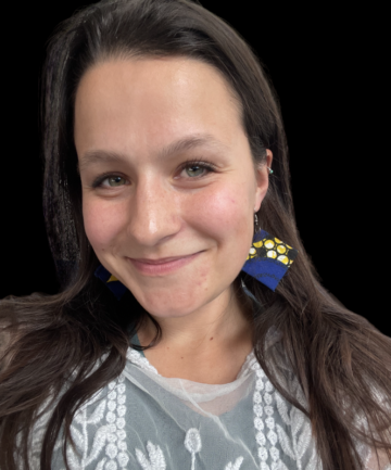 A portrait of Francesca D'Annunzio, a white woman with green eyes, long brown hair, wearing a white shirt and big blue and yellow earrings.