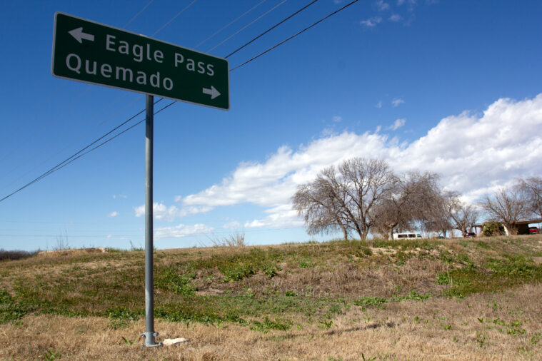 A road sign along a rural road, pointing one way to Eagle Pass, Texas and the other to Quemado, Texas.