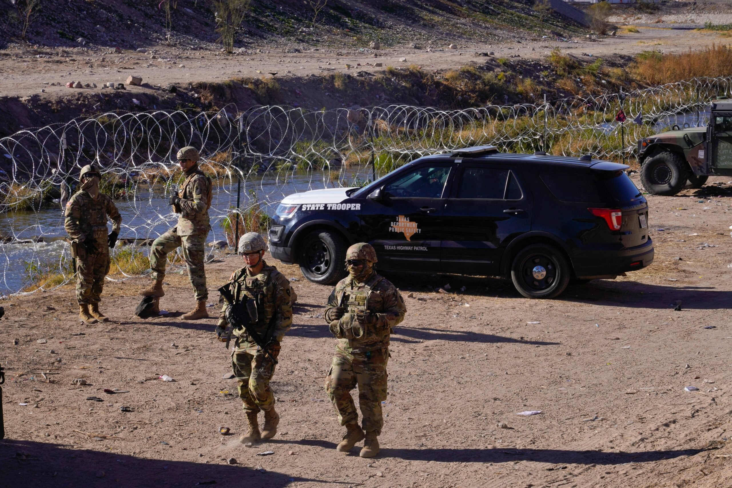 Four uniformed Texas national guard troops stand near a Texas Department of Public Safety SUV, near barbed wire which stands at the border with Mexico in El Paso.