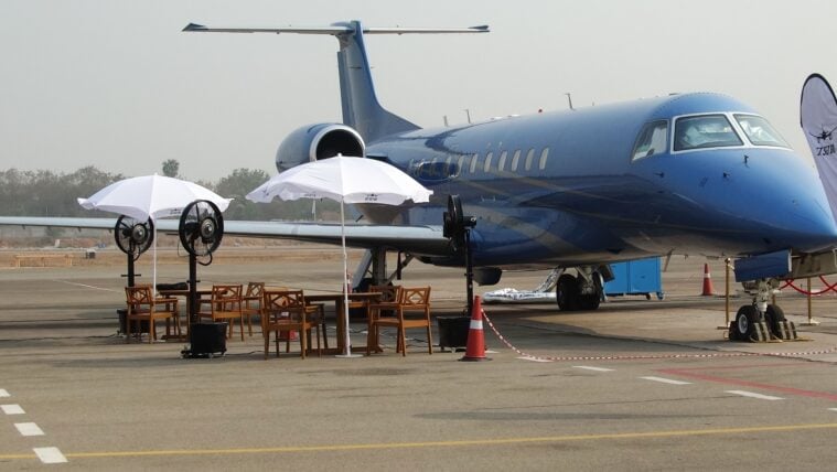 A small jet on display on a tarmac, an with umbrella-covered seating area nearby.,