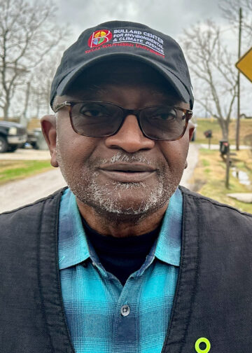 Robert D. Bullard, a Black man with light a graying beard, wearing a jacket, flannel shirt, glasses with transition lenses, and a Bullard Center ballcap.