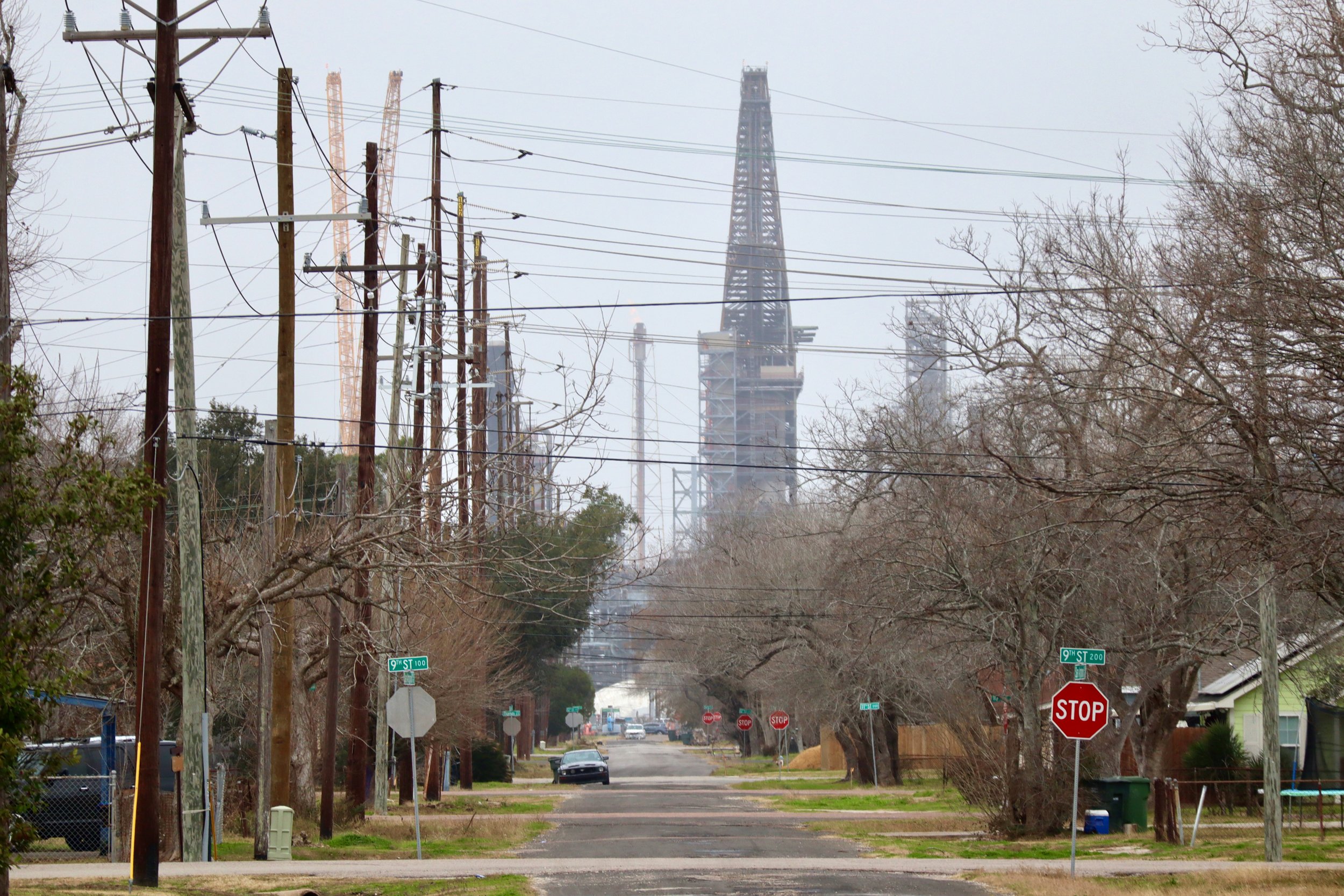 The infrastructure of an oil refinery towers over the homes and trees of a residential Texas neighborhood.