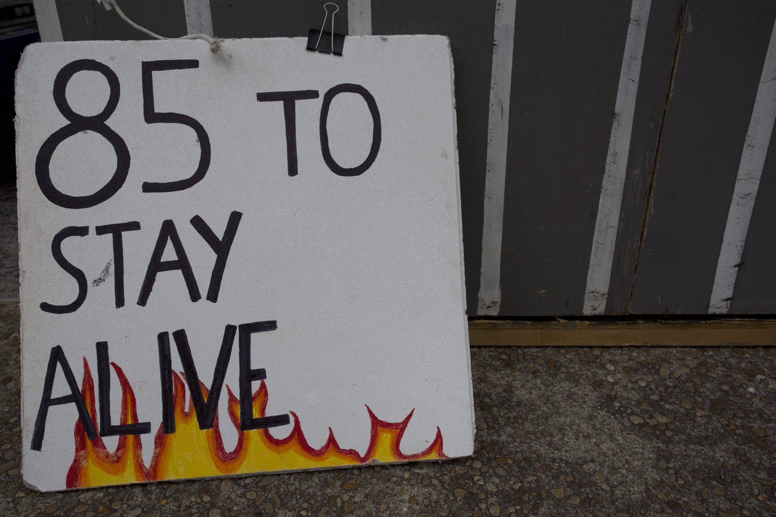 A sign with hand-drawn flames reads "85 to stay alive"