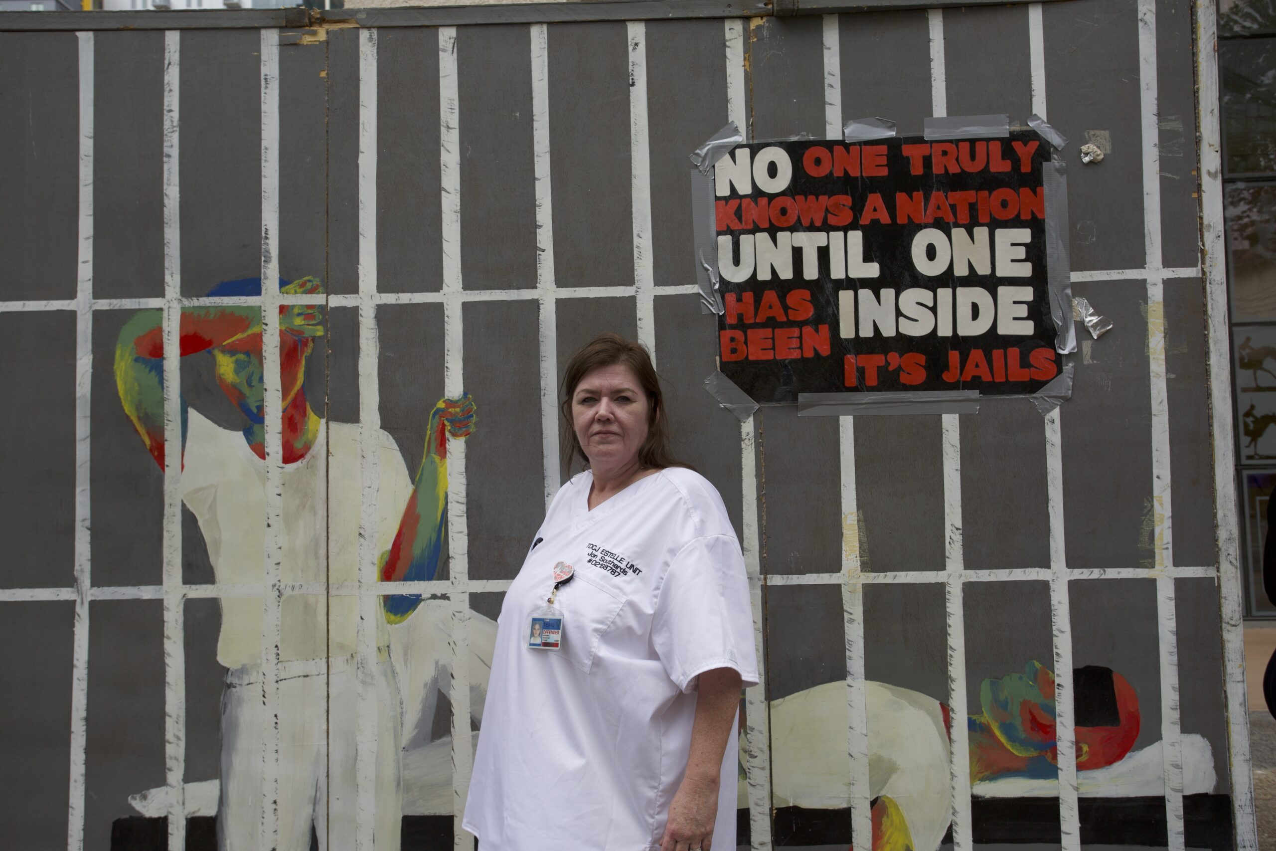 Tona Southards-Naranjo stands in front of a mural that depicts a hot prison cell. A sign reads "No one truly knows a nation until one has been inside its jails."